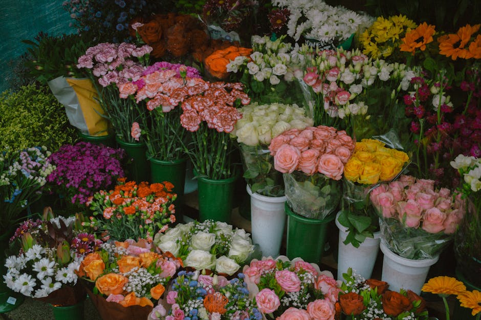 An assortment of fresh floral bouquets and potted plants arranged on display at a flower shop. The flowers include pink roses, white roses, orange and yellow roses, purple daisies, and white daisies, 